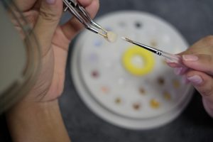 Dental technician applies ceramic material to the crown using tweezers and brush on dental palette background .Dental technology close-up